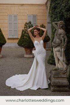 a woman in a white wedding dress standing next to a stone statue and shrubbery