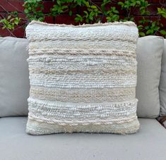 a white pillow sitting on top of a couch next to a green plant in front of a brick wall