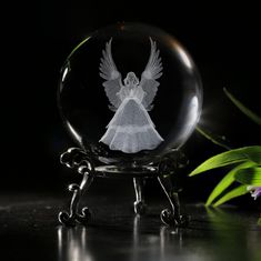 a glass ball with an angel etched on the front and side, sitting next to a plant