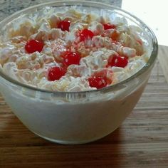 a bowl filled with fruit and cream on top of a wooden table next to a knife