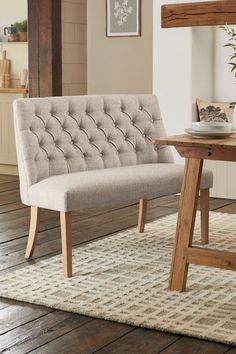 a beige bench sitting on top of a wooden floor next to a table and chair