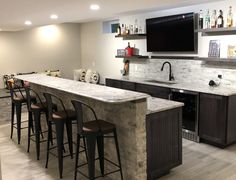 a bar with four stools and a television mounted on the wall in a basement