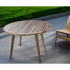 a wooden table and two chairs sitting on concrete ground next to grassy area with grass in the background