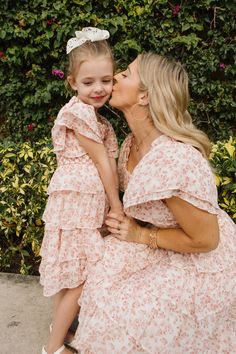 a mother and daughter kissing each other in front of bushes