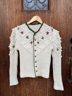 Here is a beautiful handmade  Austrian (believe Tyrolean) cardigan sweater with pewter buttons. If I am wrong on the Tyrolean please message me so I can update the listing!  Color is ivory along with green and red flowers/trim - perfect for Christmas! I am  Unsure of the yarns material and era.  This has been cleaned. As it's been formally owned and worn, mild fuzzing near hem and bottom of arm.  Please see measurements as this is handmade. Best for a smaller / petite person. The yarn expands so it gives some wiggle room.  Measurements:  Bust - 32 inches Hem - 28 inches  Length - 21.5 inches Arm - Collar to wrist - 29 inches  All sales final! For additional questions, images or issues with your order please contact me!   Vintage products may not be perfect so I give honest reviews and crit Handmade Cream Cardigan For Winter, Bohemian Winter Cardigan With Buttons, White Wool Sweater With Button Closure, Bohemian Winter Sweater With Buttons, Handmade Vintage Cardigan For Winter, Handmade Vintage Winter Cardigan, Tyrolean Cardigan, Room Measurements, Popcorn Sweater