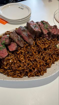 a white plate topped with meat and noodles on top of a table next to plates