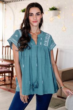 Indian artisan Anchal Ahuja creates a fresh look with this casually elegant blouse. Designed with a blend of cotton and silver-colored Lurex the short-sleeved blouse features a round neckline with two tie tassels and a loose comfortable fit. The artisan adorns the blouse with traditional Indian chikankari embroidery in a delicate floral motif then finishes the top with a teal cotton lining. Chikankari Embroidery, Teal Blouse, Top Ideas, Elegant Blouses, Floral Tunic, Streetwear Tshirt, Cotton Blouse, Fresh Look, Traditional Indian