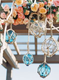 several glass balls hanging from a wooden structure with flowers on the ceiling and in the background