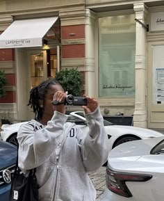 a woman taking a photo with her cell phone while standing in front of parked cars