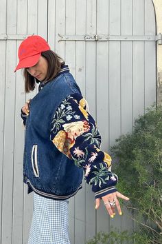 a woman wearing a red hat and blue jean jacket is holding her hand out to the side