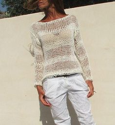 a woman standing in front of a wall wearing white pants and a knitted sweater