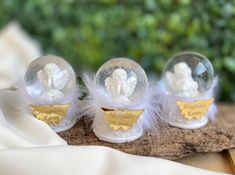 three glass balls with white feathers and angel designs on them sitting on a piece of wood