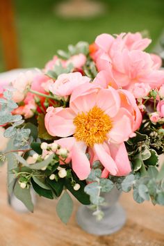 a vase filled with lots of pink flowers on top of a wooden table covered in greenery