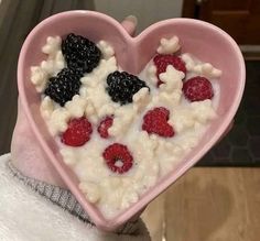 a pink heart shaped bowl filled with cereal and berries