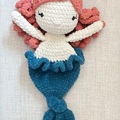 a crocheted mermaid doll laying on top of a white sheet with pink hair