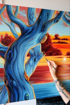 a person is painting a tree with blue paint on the ground and red clouds in the background