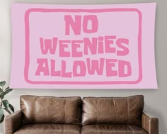 a pink sign that says no weenies allowed on the wall above a brown leather couch