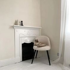 a cat sitting on a chair in front of a fire place with a white fireplace