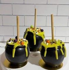 three black pots with yellow icing and sprinkles on them sitting on a white surface