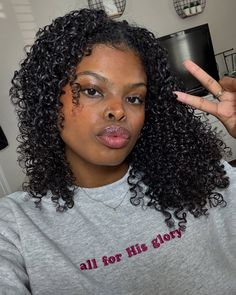 a woman with long curly hair making the peace sign for her glory written on her t - shirt