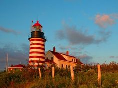 a red and white lighthouse sitting on top of a lush green hillside next to a house