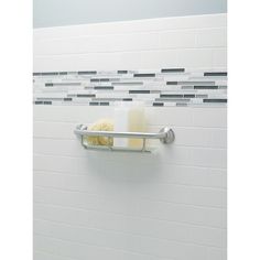 a bathroom with white tile walls and silver metal shelf holding soap, scrubber and lotion