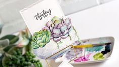 a card with succulents on it is sitting next to a plate and plant