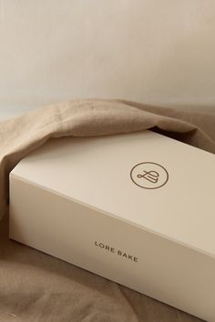 a white box with a brown logo on it sitting on top of a bed next to a pillow