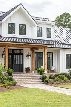 a white house with black doors and steps leading up to the front door is surrounded by greenery