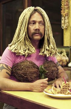 a man with dreadlocks sitting at a table in front of a plate of food