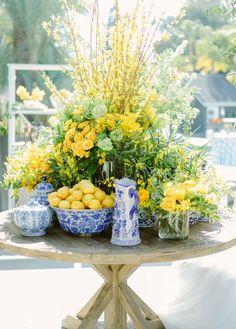 a table topped with blue and white vases filled with yellow flowers next to lemons