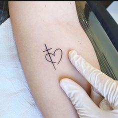 a person with a tattoo on their arm holding up a heart and cross in the middle