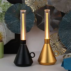 two black and gold lamps sitting next to each other on a white table with plates in the background