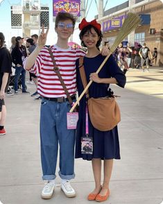 two people dressed up in costumes and holding brooms at an outdoor event with other people standing around