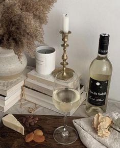 a glass of white wine next to a bottle of wine and some cheese on a table