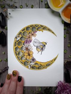 a person holding up a card with a bee on the moon and flowers around it