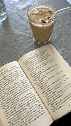 an open book sitting on top of a table next to a glass filled with liquid