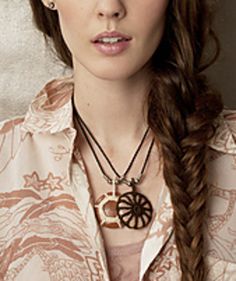 a woman with long hair wearing a shirt and necklace, looking at the camera while standing in front of a wall