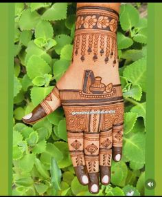 a hand with henna on it and green leaves in the background, showing an intricate design