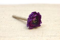 a single purple flower sitting on top of a piece of cloth next to a needle