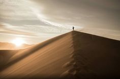 a lone person standing on top of a sand dune in the middle of the desert