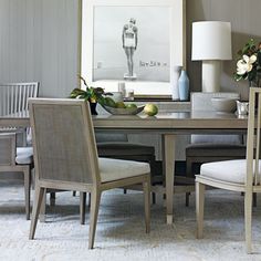 a dining room table with chairs and a vase on it's side, in front of a framed photograph