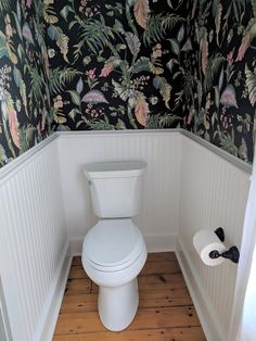 a white toilet sitting inside of a bathroom next to a wall papered with flowers