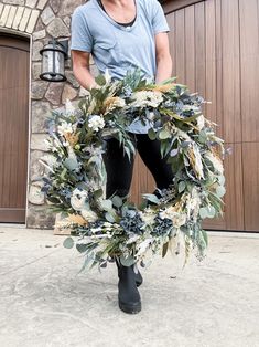 a man standing in front of a garage holding a wreath with flowers and leaves on it