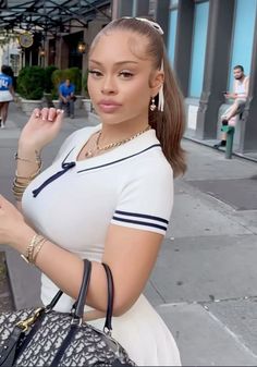 a woman is standing on the sidewalk holding a purse and looking at her cell phone