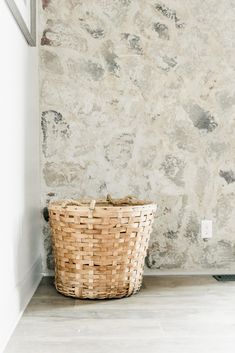 a wicker basket sitting on the floor in front of a wall with a stone background