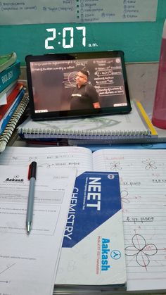 a laptop computer sitting on top of a desk next to a pile of books and notebooks