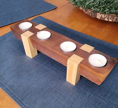 three white candles are sitting on a wooden table with blue place mats and a potted plant in the background