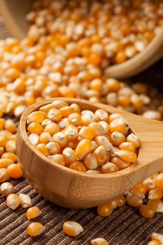 a wooden spoon filled with corn on top of a table