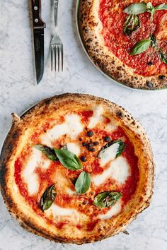 two pizzas with basil and mozzarella on them next to a fork and knife